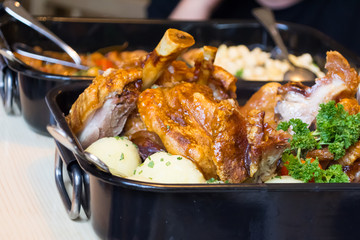 Barbecued chicken leg with boiled potatoes and vegetables in baking dish, closed up. Traditional dinner in bavarian restaurant