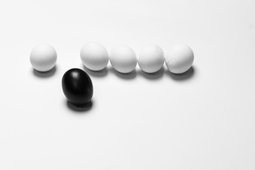 on a white background, white eggs in a row and one black symbolizing diversity, separation, concretion and leadership