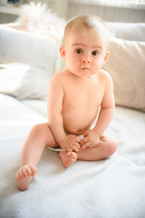 Cute baby girl sits straight on couch in diaper 8th month