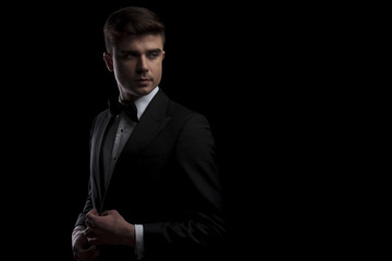 elegant man buttons his black tuxedo and looks to side