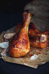 Roasted chicken drumsticks with garlic on black background close up