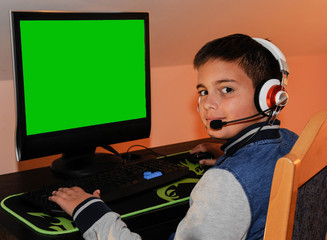 A young gamer boy playing video games on computer wearing headphones and colorful keyboard