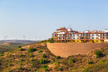 Apartments built high on a hillside in Costa Esuri an urbanisation in Ayamonte, Alongside the River Guadiana in Andalusia, Spain. Turbines in a wind farm can be seen on the hillside