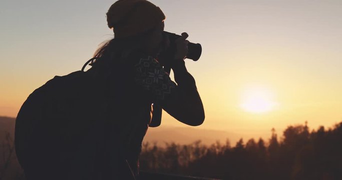 Young Woman Taking Pictures of Sunlit Fall Mountain Landscape form the Top. SLOW MOTION. Hiker Girl is Taking photos with digital camera of beautiful autumn hills landscape at sunset, Lens Flare.  