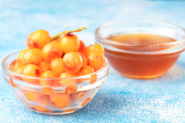 Sea-buckthorn berries in bowl and natural honey or sea buckthorn oil on blue background