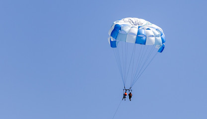 Couple parasailing with a blue and white parachute against a clear blue sky in the Riviera Maya Mexico