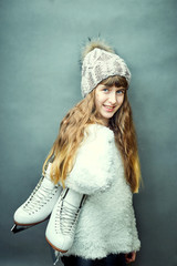 A girl with skates in her hands in a white sweater and hat.