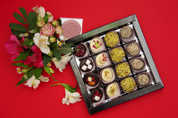 sweets made of white and dark chocolate in a box decorated with fresh flowers on a red background