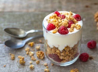 Fototapeta na wymiar White yogurt with muesli in glass bowl with pieces raspberries on top on natural wooden desk.
