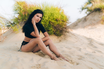 Obraz premium The concept of leisure, fashion, beachwear, travel, nature, people. Attractive brunette model in a fashionable swimsuit posing on the sand for a magazine. Copyspace on swimwear.