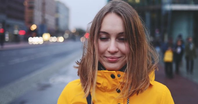 Portrait of Woman Standing on the Wind in Big City. SLOW MOTION 4K. Young Woman in Berlin waiting near the busy road. Breeze is playing with girls hair. Stormy weather, autumn, winter, spring.