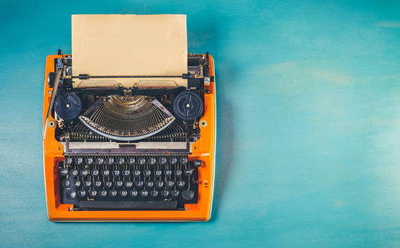 Fototapeta Workspace with orange vintage typewriter on blue wooden table background, toned