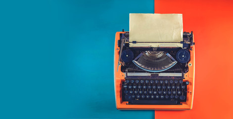 Workspace with orange vintage typewriter on blue and orange background, toned