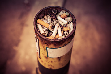 Ashtray at the smoking place, full of the variety of cigarettes after smoked. Dark toned