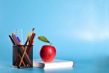 School supplies pencils, pens, ruler, brush , books and apple on a blue background with a place for text
