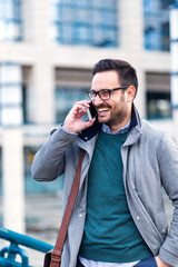 Happy young businessman talking on mobile phone near business center