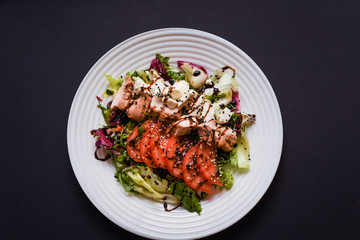 Meat salad with tomato served in white plate on dark table. Copy space