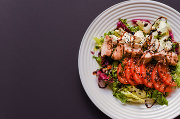 Meat salad with tomato served in white plate on dark table. Copy space