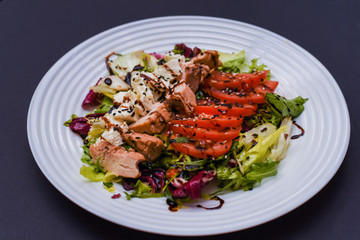 Meat salad with tomato served in white plate on dark table. Copy space