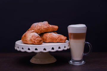 Coffee relax time. Latte with croissant on black background. Copy space.