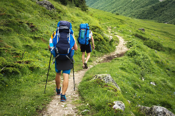 Hiking trail in Svaneti region, Georgia. Two hikers men walk on trek in mountain. Tourists with backpacks hike in highlands. Trekking in mountains. Hills and mounts in sport tourism