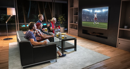 Group of fans are watching a soccer moment on the TV and celebrating a goal, sitting on the couch in the living room.