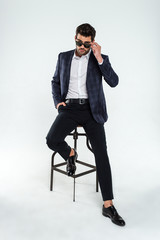  What I see here? Full length of handsome young man adjusting his sunglasses and looking at camera while sitting against white background