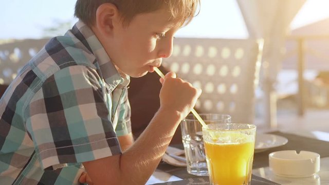 Cute little boy drinking fresh orange juice from glass in city cafe