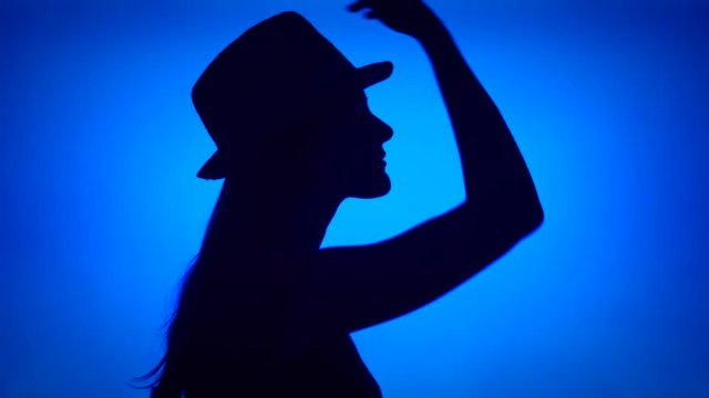 Silhouette of young woman putting on hat on head. Female's face in profile with headwear on blue background. Black contour shadow of teenager's half-face