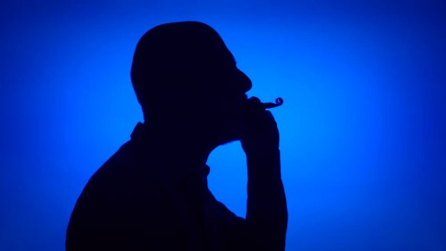Silhouette of senior man using birthday whistle on blue background. Male's face in profile celebrating. Black contur shadow of grandfather's half-face. Celebration concept