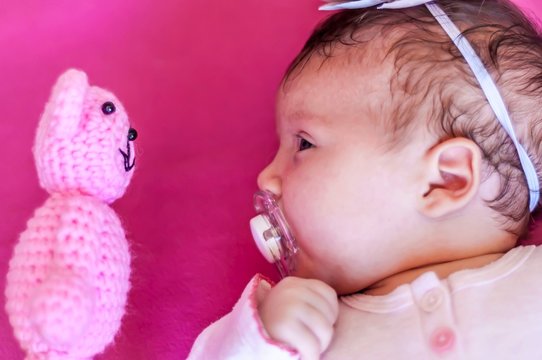 Funny picture of a Caucasian newborn infant baby girl looking at the teddy bear face to face. Discover the new world concept, learning new things. One month old child.