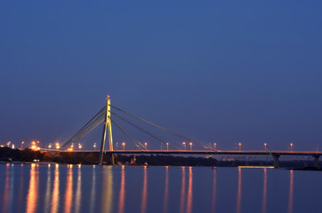 Bridge at night beside the Dnipro river with reflection in water