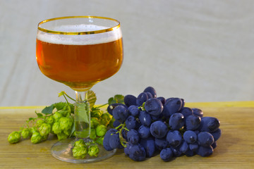 a beautiful glass of warm beer with a bunch of grapes and fresh hops