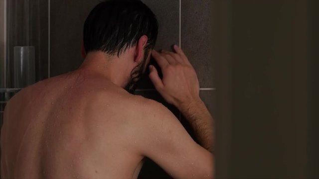 A STATIC CLOSE UP SHOT Through An Open Door, Of An Emotional And Sad Man With His Hand On The Wall, Wiping His Tears And Banging His Fist And Head, Whilst Showering.