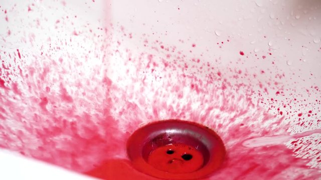 Red and colored paint being poured into sink with a dirty grimey drain piece close up in a bathroom