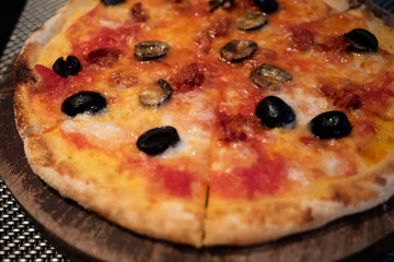 Delicious, cheesy and freshly baked Italian Pizza Margherita topped with olive, mozzarella and Parmesan cheese on a wooden board by professional pizza chef. Selective focus.