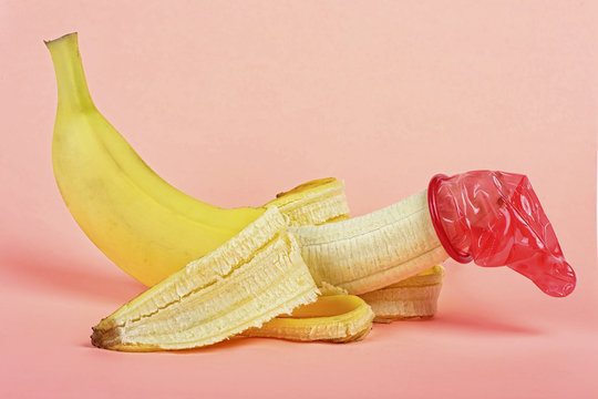 Red condom on yellow banana, pink background.
