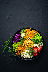Bowl dish with brown rice, cucumber, tomato, green peas, red cabbage, chickpea, fresh lettuce salad and cashew nuts. Healthy balanced eating