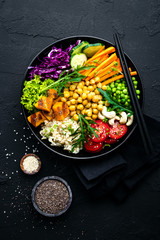 Bowl dish with brown rice, cucumber, tomato, green peas, red cabbage, chickpea, fresh lettuce salad and cashew nuts. Healthy balanced eating