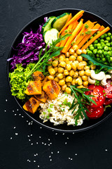 Bowl dish with brown rice, cucumber, tomato, green peas, red cabbage, chickpea, fresh lettuce salad and cashew nuts. Healthy balanced eating