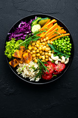 Bowl dish with brown rice, cucumber, tomato, green peas, red cabbage, chickpea, fresh lettuce salad and cashew nuts. Healthy balanced eating