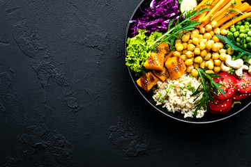 Bowl dish with brown rice, cucumber, tomato, green peas, red cabbage, chickpea, fresh lettuce salad and cashew nuts. Healthy balanced eating