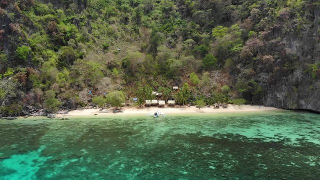 Aerial tilt drone shot flying over clear, shallow, blue water and tilting down towards a paraw boat at a private beach, at Coron island, in Philippines, Asia