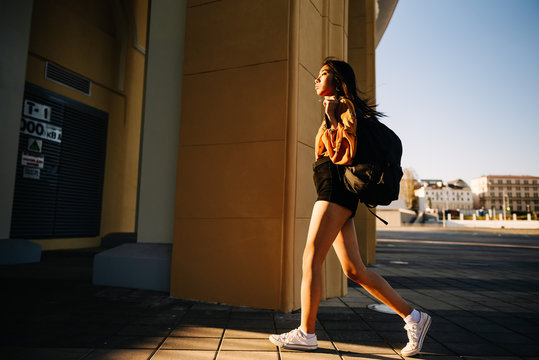 Asian Beautiful Woman With Black Hair, Yellow Shirt, Black Shorts, Outdoor Resting, Looking At Camera. Portrait Young Girl In An Urban Environment.