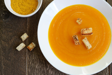 Pumpkin soup in a white plate with croutons and curry seasoning