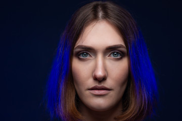 Fototapeta premium Art portrait of a girl on a black background with blue neon lights of hair. Beautiful eyes, natural beauty, clean skin, facial and hair care. MAKEUP concept. A large plan