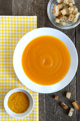 Pumpkin soup in a white plate with croutons and curry seasoning