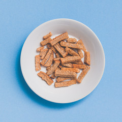 Crispy rusk on white plate, beer snack. Top view on blue background