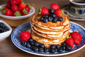 Stack of pancakes with blueberries and strawberries on a blue and white plate with bowls of...