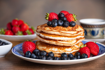 Stack of pancakes with blueberries and strawberries on a blue and white plate with bowls of...